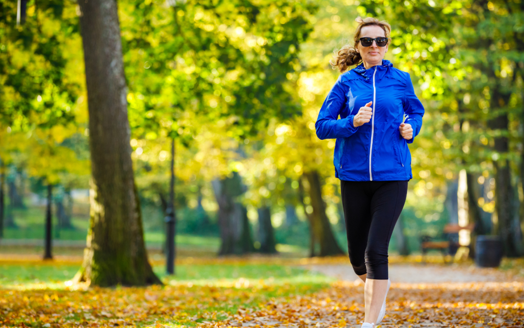 woman running in blue coat and black trousers in the park on a sunny autumn day